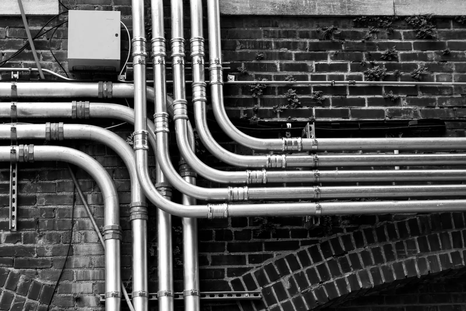 Stainless conduit runs sweeping across a brick wall, in black and white.